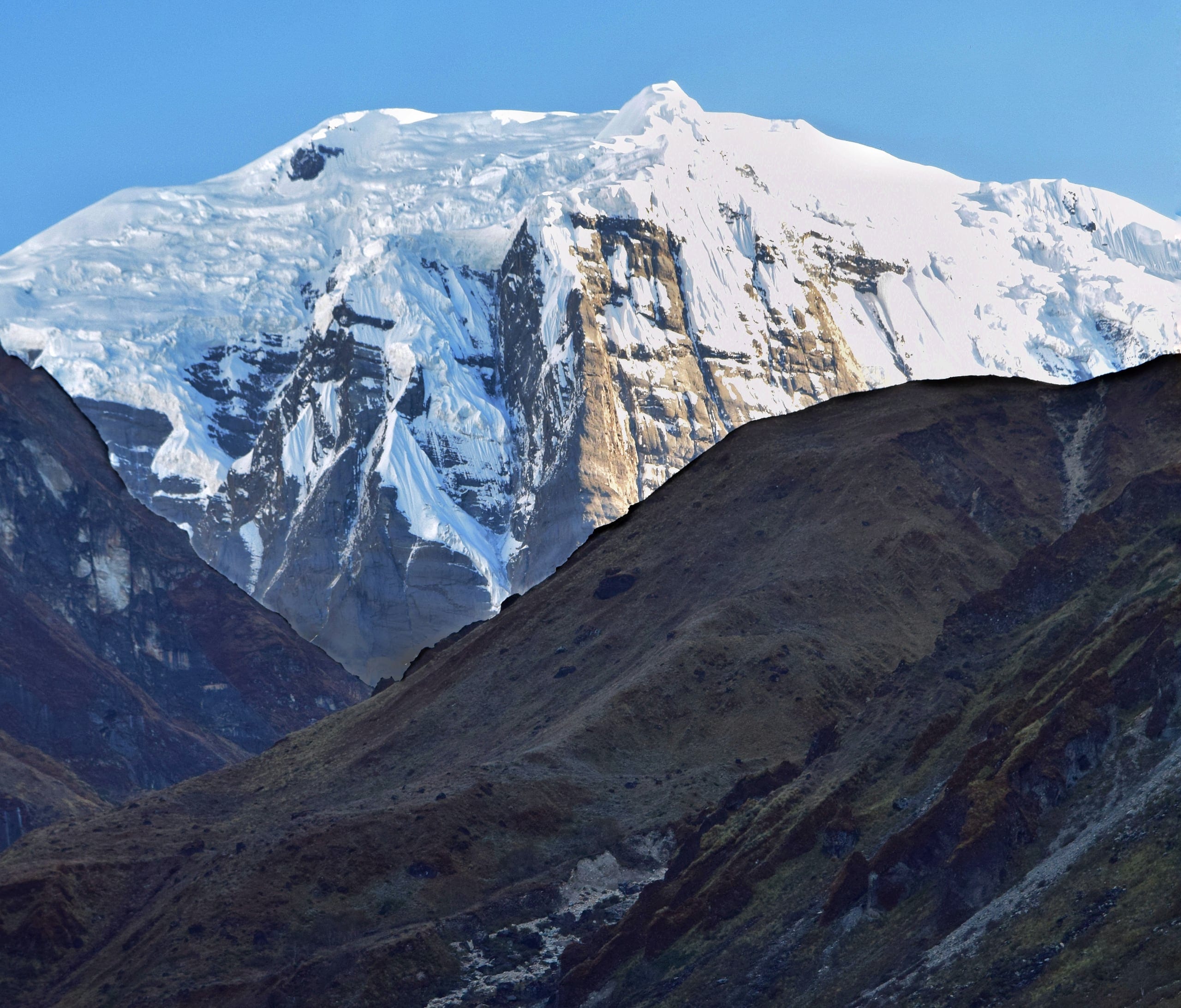 The snow-covered north face of Annapurna I rising behind a dark ridge